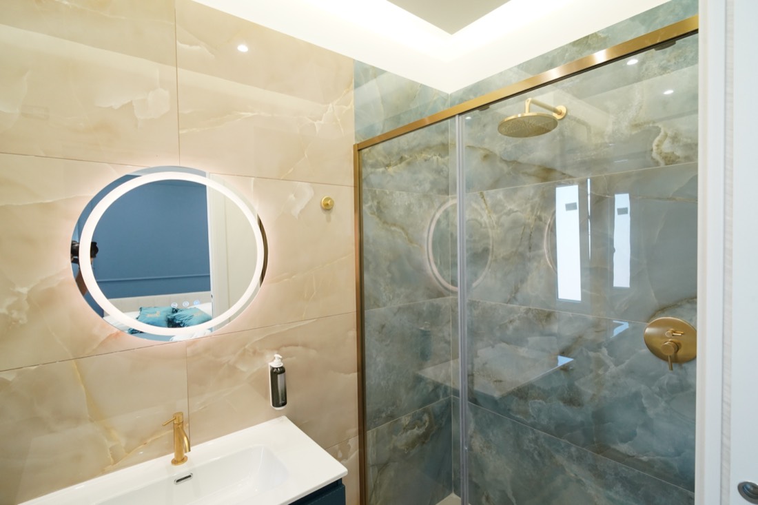 Bagno con doccia a filo pavimento, marmo onice blu e specchio tondo