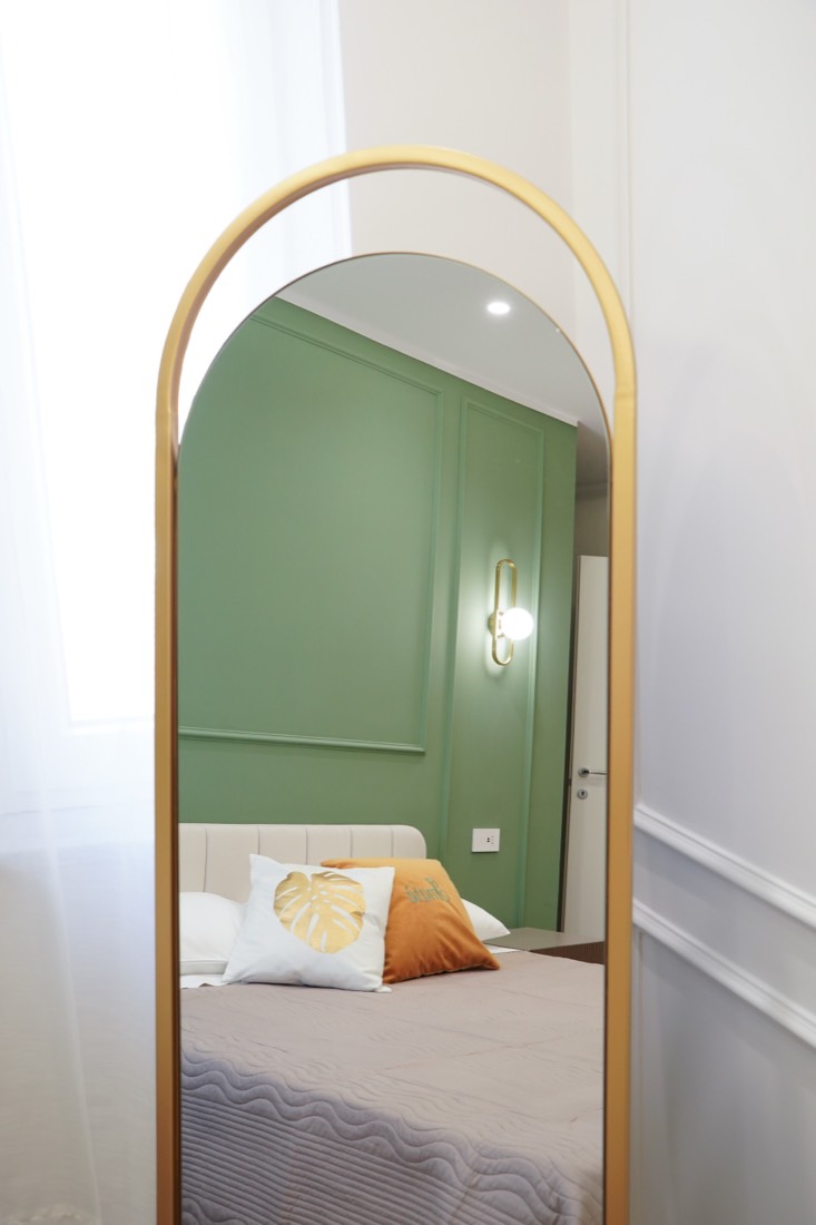 Specchio ad arco dorato che riflette la camera con boiserie verde