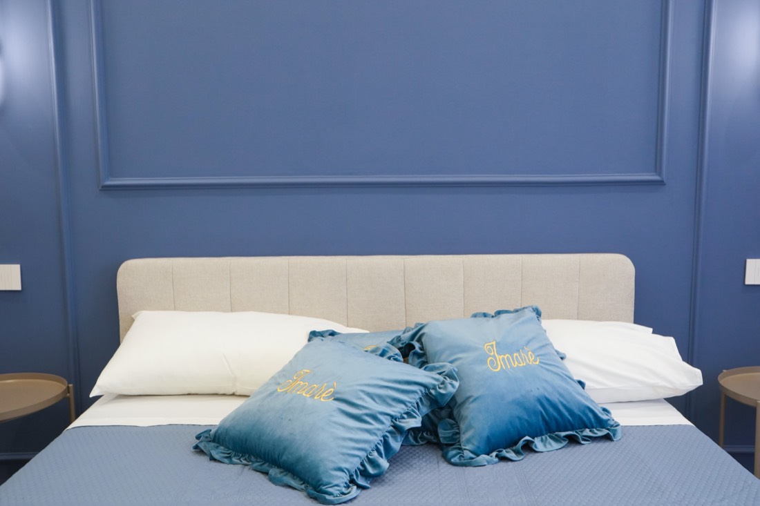 Cuscini in velluto blu ricamati con il marchio Imarè sul letto