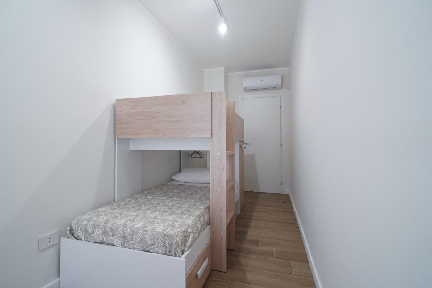Camera con letto a castello in legno chiaro, armadio, TV a parete e aria condizionata