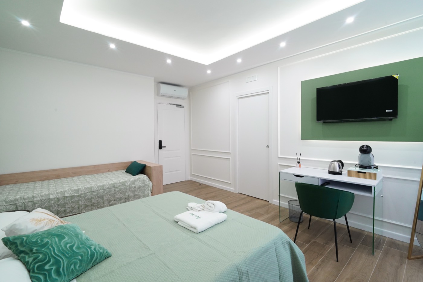 Camera Verde Superior: letto matrimoniale più letto singolo, pannello verde con TV, scrivania e finestra sul balcone